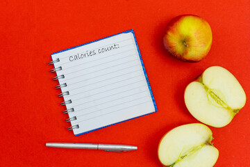 Calories written in a diary on red background with sliced apples. Calorie counting concept.