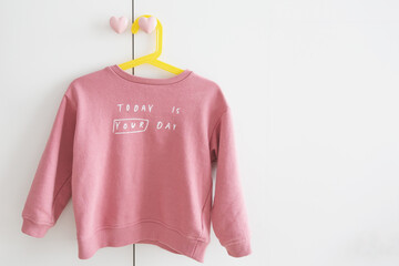 one children's pink sweater hangs on a yellow hanger on a white wardrobe with heart handles with the inscription today is your day, place for text