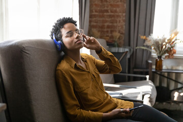 Tranquil peaceful young Black girl enjoying relaxing music for meditation, mindfulness, recreation, practicing stress relief techniques, resting on comfortable couch at home with closed eyes