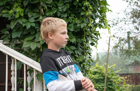a boy stands on a wooden porch in the village and looks into the distance