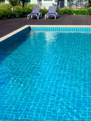 Fototapeta na wymiar Swimming pool with clean clear water, vertical style, nobody. Square shaped pool with blue tiles with sunbeds on the wood decks, no people. water surface. Overhead view. Summer background.