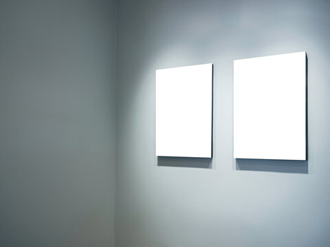 Two mockup vertical rectangle painting frames hanging on white wall background at the room corner with copy space. Blank white canvas frame with empty space in gallery, minimal style.