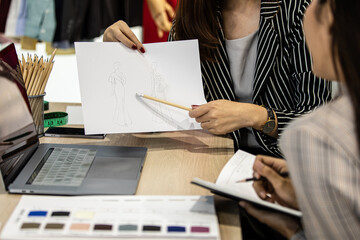 Unrecognizable woman showing and presenting paper with fashion design sketch to another woman in office.