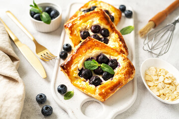 Mini puff pie with cheese cream, almonds, and blueberries in a plate on the kitchen table. Delicious layered square with berries, dorblue or ricotta, nuts on a culinary background