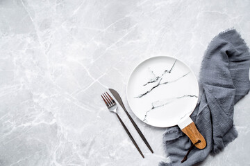 Banner. An empty ceramic marble plate with a wooden handle, a fork, a knife and a towel against the background of a gray concrete table. Space for text. Menu concept for cafes and restaurants.