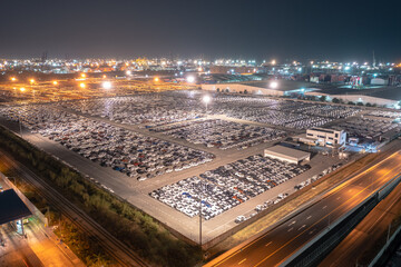 New cars parked at distribution center automobile factory at night with lights. aerial view