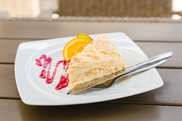 Layered cake with cream Napoleon millefeuille vanilla slice with red jam and fruits on wood background, selective focus, food or menu concept
