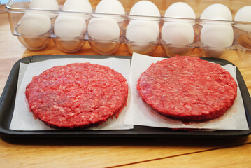 Fresh Raw Hamburger Patties with Raw Eggs in the Background