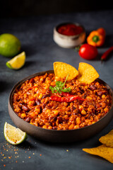 Mexican hot chili con carne in a bowl with tortilla chips on dark background