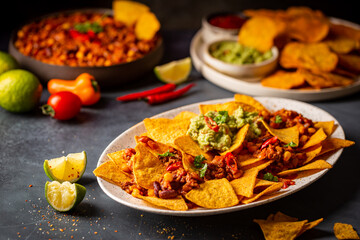 Delicious plate of yellow corn nachos chips with cheese, minced meat and red hot spicy salsa over...