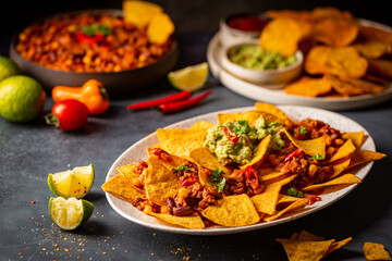 Delicious plate of yellow corn nachos chips with cheese, minced meat and red hot spicy salsa over dark background
