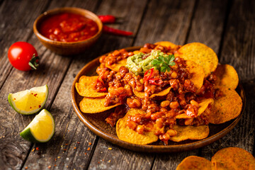 Delicious plate of yellow corn nachos chips with cheese, minced meat and red hot spicy salsa over wooden table