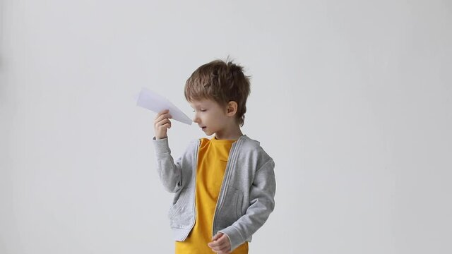 Cute little boy launched a paper plane to fly on white background at home, expressing happiness and positive emotion