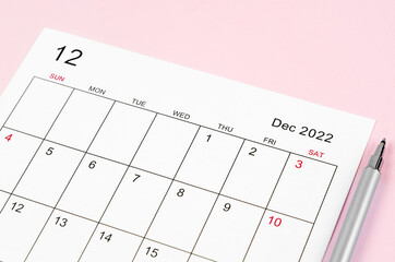 December 2022 calendar sheet with pen on pink background.