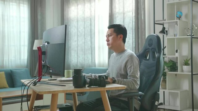 Asian Cameraman In Long Sleeved T-Shirt And Black Pants Being Tired While Using Desktop Computer For Working At Home.
