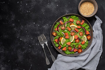 Salad with salmon and fresh vegetables on a black concrete background. Top view, flat lay, copy space.
