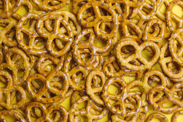 pile of salty mini pretzels on a yellow background. Popular beer snack. Background of baked salted pretzels. Top view