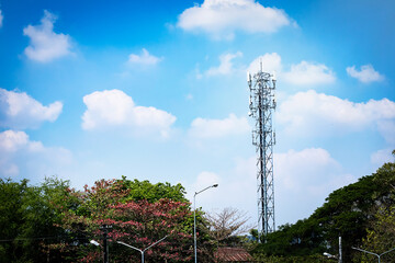 a transmitter pole on the small forest with a villa below a blue sky.