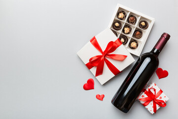 Fototapeta na wymiar Bottle of red wine on colored background for Valentine Day with gift and chocolate. Heart shaped with gift box of chocolates top view with copy space