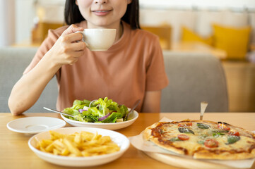 A woman drinking coffee with feeling happy and enjoy to eat food in the restaurant in leisure time. dine in the restaurant, eating delicious served hot pizza and salad. Eating concept. Italian food.
