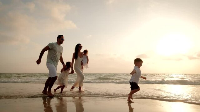 Happy Cheerful Family Running On The Beach At A Beautiful Sunset. Wide Shot