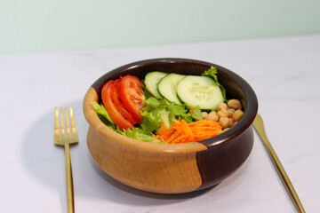 colorful salad with cucumber, tomato, carrot, onion, lettuce and chickpeas in a wooden bowl with golden knife, fork and spoon