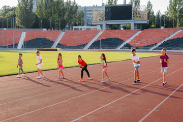 A large group of children, boys and girls, run and play sports at the stadium during sunset. A healthy lifestyle.