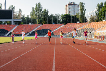 Obraz premium A large group of children, boys and girls, run and play sports at the stadium during sunset. A healthy lifestyle.