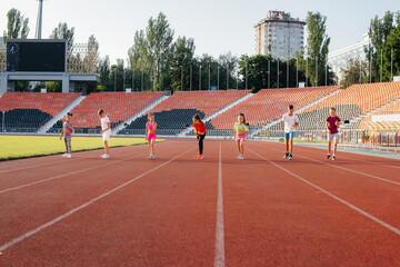 Fototapeta premium A large group of children, boys and girls, run and play sports at the stadium during sunset. A healthy lifestyle.