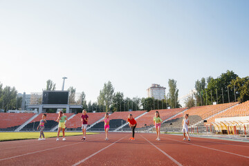 A large group of children, boys and girls, run and play sports at the stadium during sunset. A healthy lifestyle.