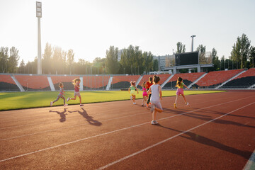 Obraz premium A large group of girls, got ready at the start before running at the stadium during sunset. A healthy lifestyle.