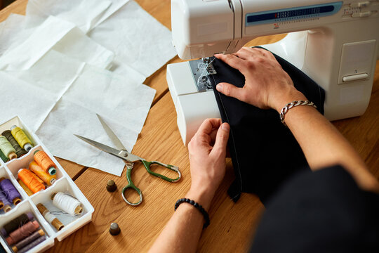 Man sews clothes on sewing machine,  male tailor working with sewing in atelier, textile industry, hobby, workspace, small busines. Creation process DIY, Workplace of seamstress.