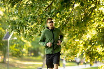 Athletic young man running while doing workout in sunny green park