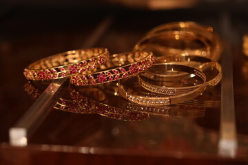 pink ruby studded multiple gold bangles with reflections on a glass table.