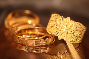 set of bold gold bangles and set of thin gold bangles with the reflection of it on a glass top