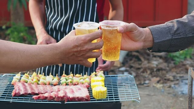 Young men cheers for a drink at a BBQ party between friends. Food, drink, people and family time concept.