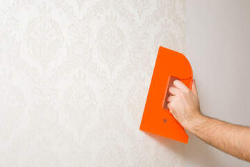 Young adult man hand using orange plastic spatula and smoothing surface from air bubbles or creases...