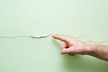 Young adult male hand finger pointing to green wall in house. Building problem and solution...