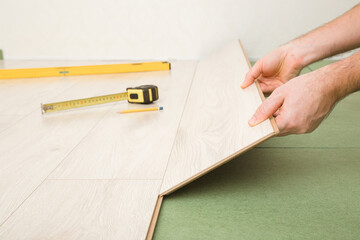 Young man hands laying light color laminate on green natural wood fiber insulation board. Flooring installation on fibreboard underlay. Repair work of home. Renovation process. Closeup. Side view.