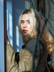 Obraz premium Young woman with blonde hair with window behind portrait