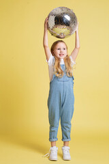 Baby girl with blonde hair isolated on yellow with a ball