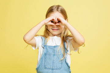 Little european baby girl with blonde hair isolated on yellow showing heart by hands