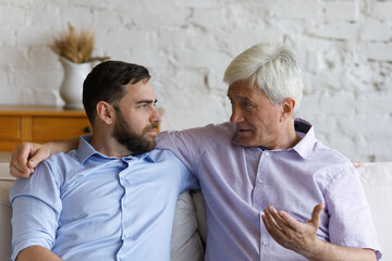 Elder grey haired loving father giving support and advice to grownup son. Senior parent and adult...