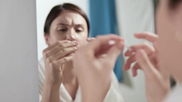 The woman wooden ear stick broke while cleaning her ears. A beautiful girl in white terry bathrobe frowns looking at herself in mirror. Disadvantages of wooden ear sticks.
