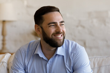 Cheerful bearded millennial man home head shot portrait. Cheerful guy, homeowner, tenant posing in apartment. Businessman entrepreneur looking away, laughing, smiling, thinking of future vision © fizkes