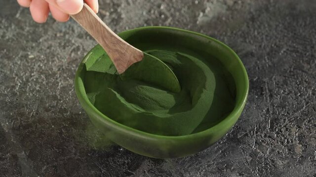Pouring green chlorella algae powder into a bowl, slow motion