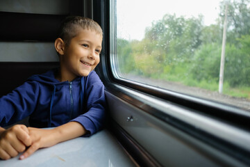 Child go the train at the window. Little passenger looks at the railway. Boy travels.