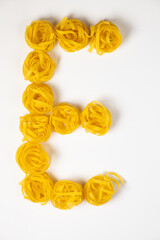 few homemade fettuccine nest in the shape of the letter E isolated on white background