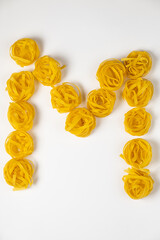 few homemade fettuccine nest in the shape of the letter M isolated on white background
