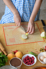 A young girl cooks at the table, in a plaid dress. Rustic home warm photo.